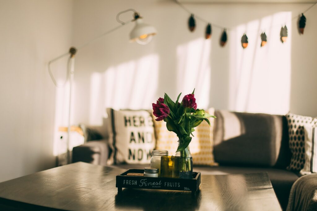 un bouquet de fleurs est posé sur une table basse dans un salon. En arrière-plan, un canapé et des coussins, une lampe.