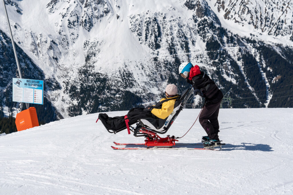 Une personne ayant un handicap pratique le handiski avec un accompagnateur, à Pralognan-la-Vanoise (73) activité hiver handicap © PY. Duval_Auvergne-Rhône-Alpes Tourisme